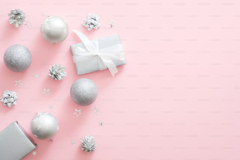 Decorazioni natalizie in argento, palline, confezione regalo, pigne su sfondo rosa pastello. Composizione minimale natalizia con arredamento moderno e lussuoso. Posa piatta, vista dall'alto, spazio di copia