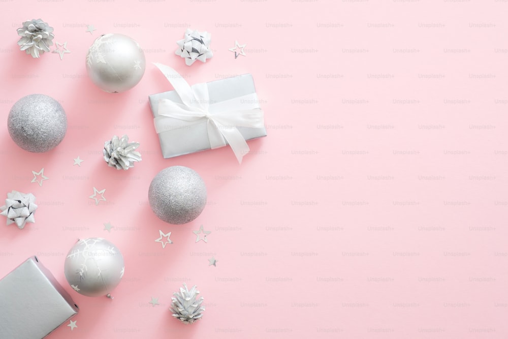 Silver Christmas decorations, balls, gift box, pine cones on pastel pink background. Xmas minimal composition with modern luxury decor. Flat lay, top view, copy space