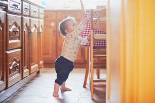 부엌 바닥에 서서 가구를 잡고 있는 소녀. 집에서 놀고 있는 어린 아이