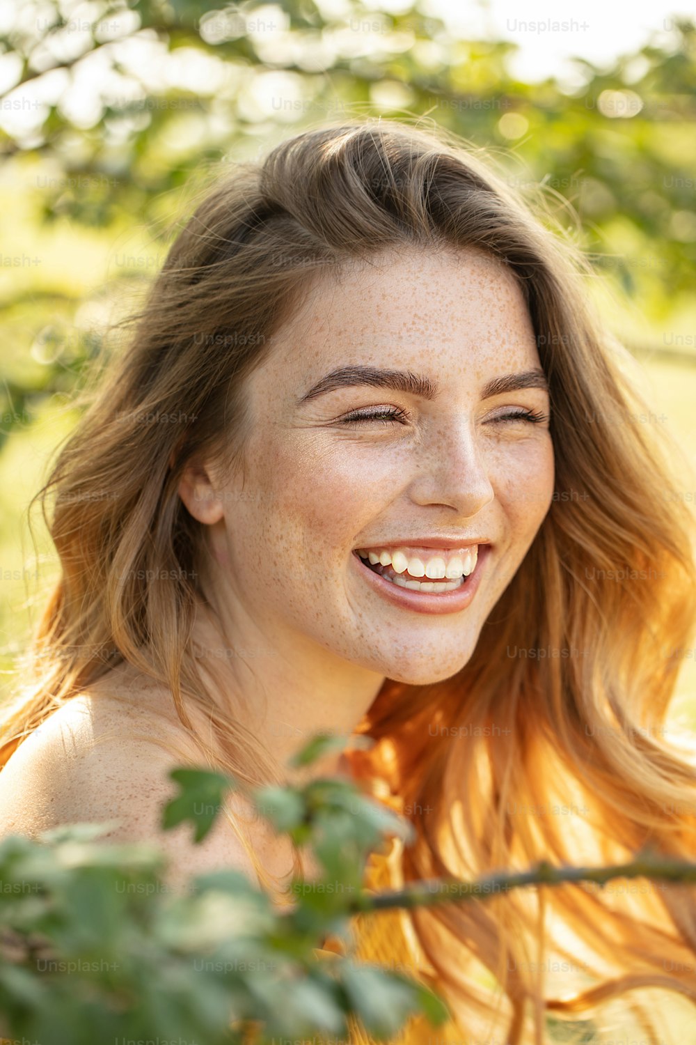 주근깨가 있는 행복한 아름다운 여자가 웃고 있고, 화창한 날에 피는 정원에서 포즈를 취하고 있다.