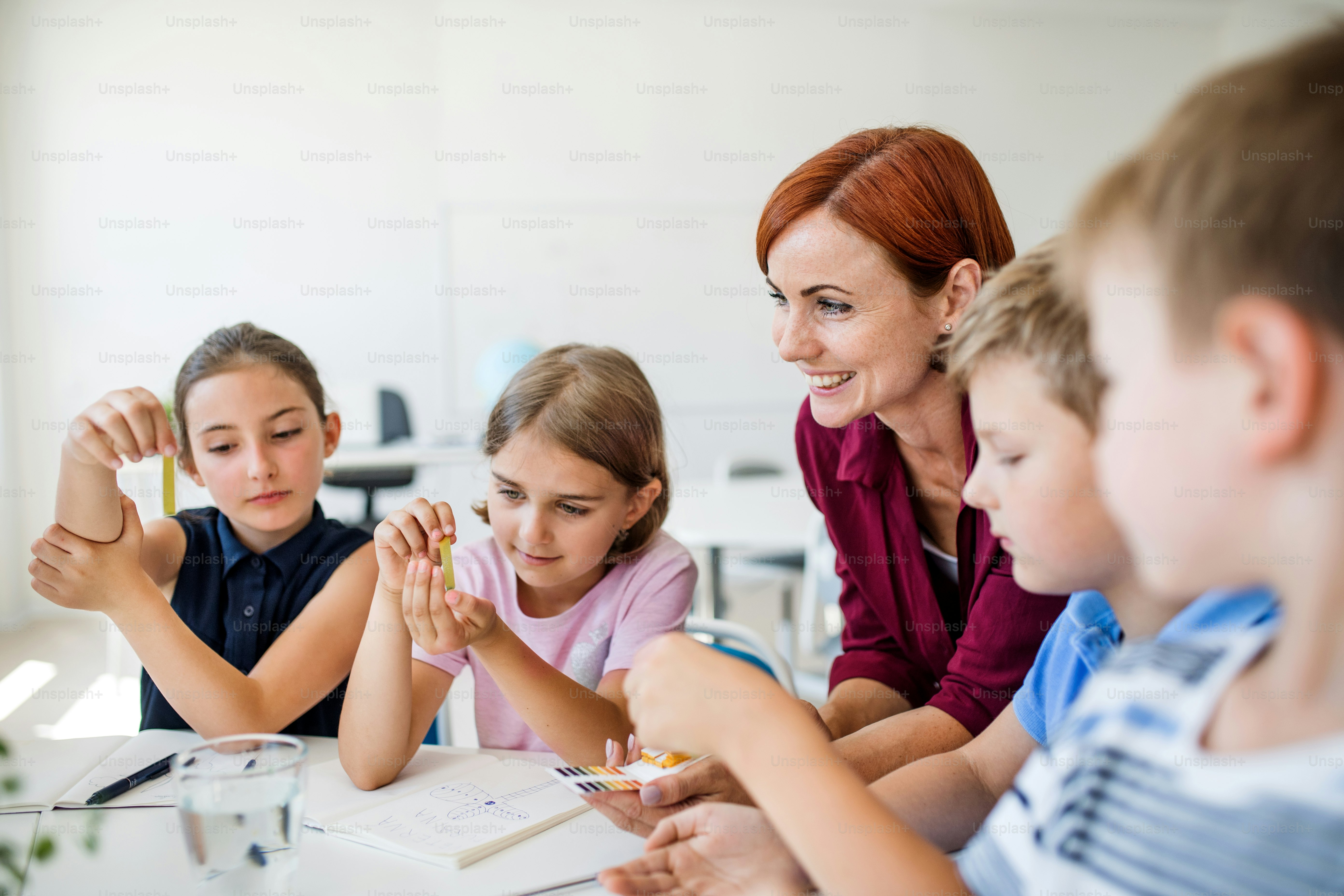 Un grupo de niños pequeños de la escuela con un maestro sentado en el suelo en clase, aprendiendo ciencias