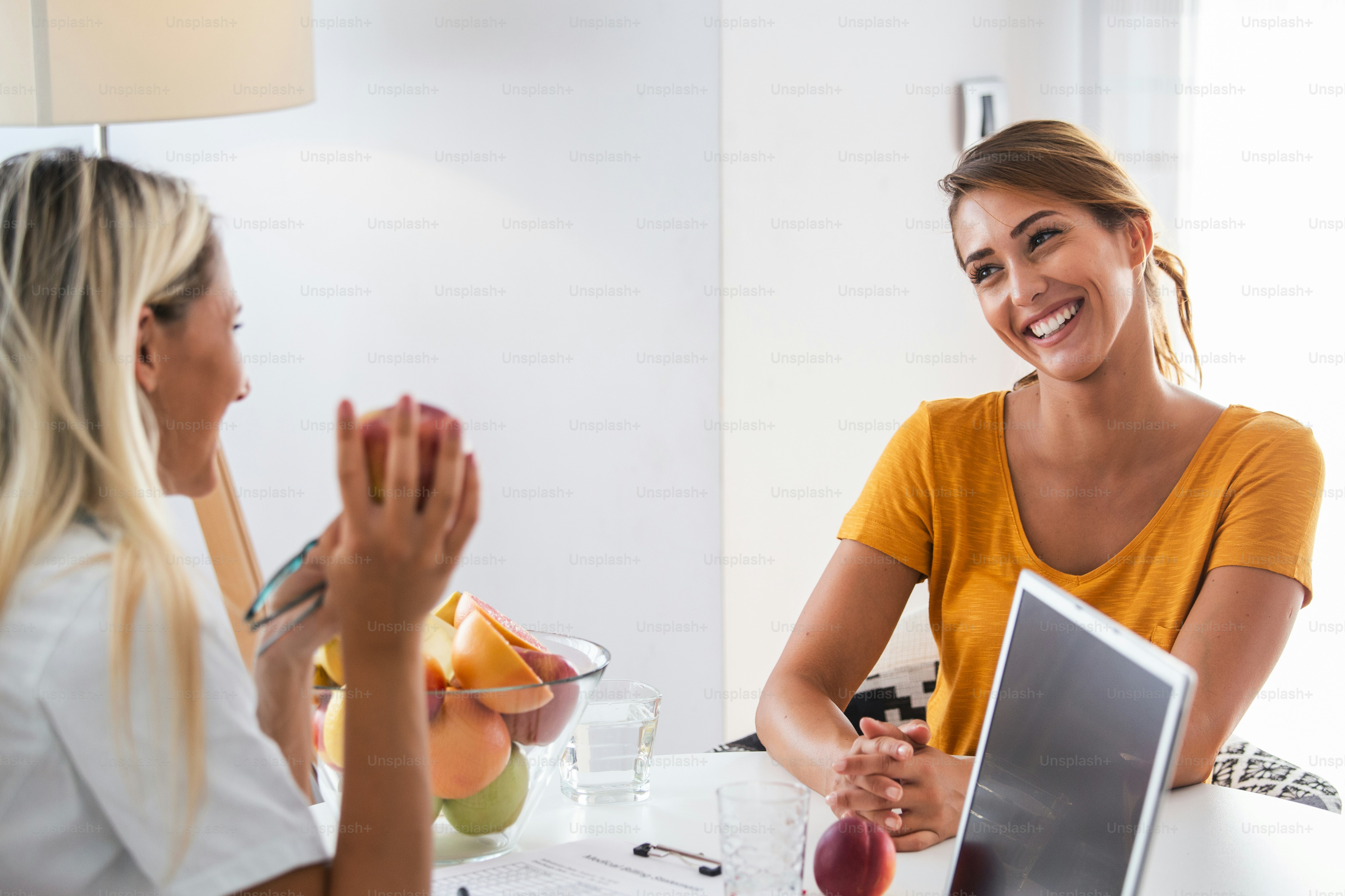 Doctor nutritionist, dietician and female patient on consultation in the office. young smiling female nutritionist in the consultation room. Nutritionist desk with healthy fruit and measuring tape.