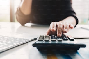 Close up Business woman using calculator and laptop for do math finance on wooden desk in office and business working background, tax, accounting, statistics and analytic research concept