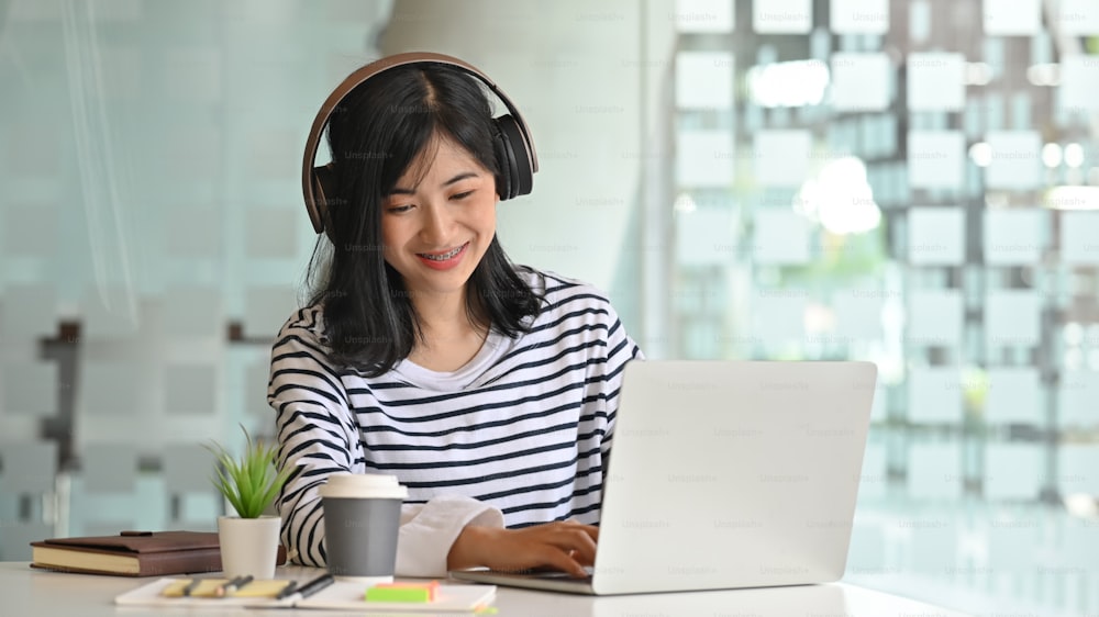 Young women using laptop and listening song in headphones.