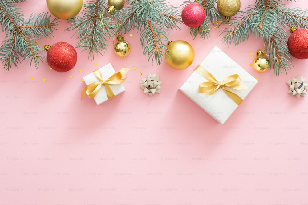 Christmas holiday composition. Xmas tree fir branches, colorful balls, gifts box on pastel pink background. Christmas, winter, New Year concept. Flat lay, top view, overhead.