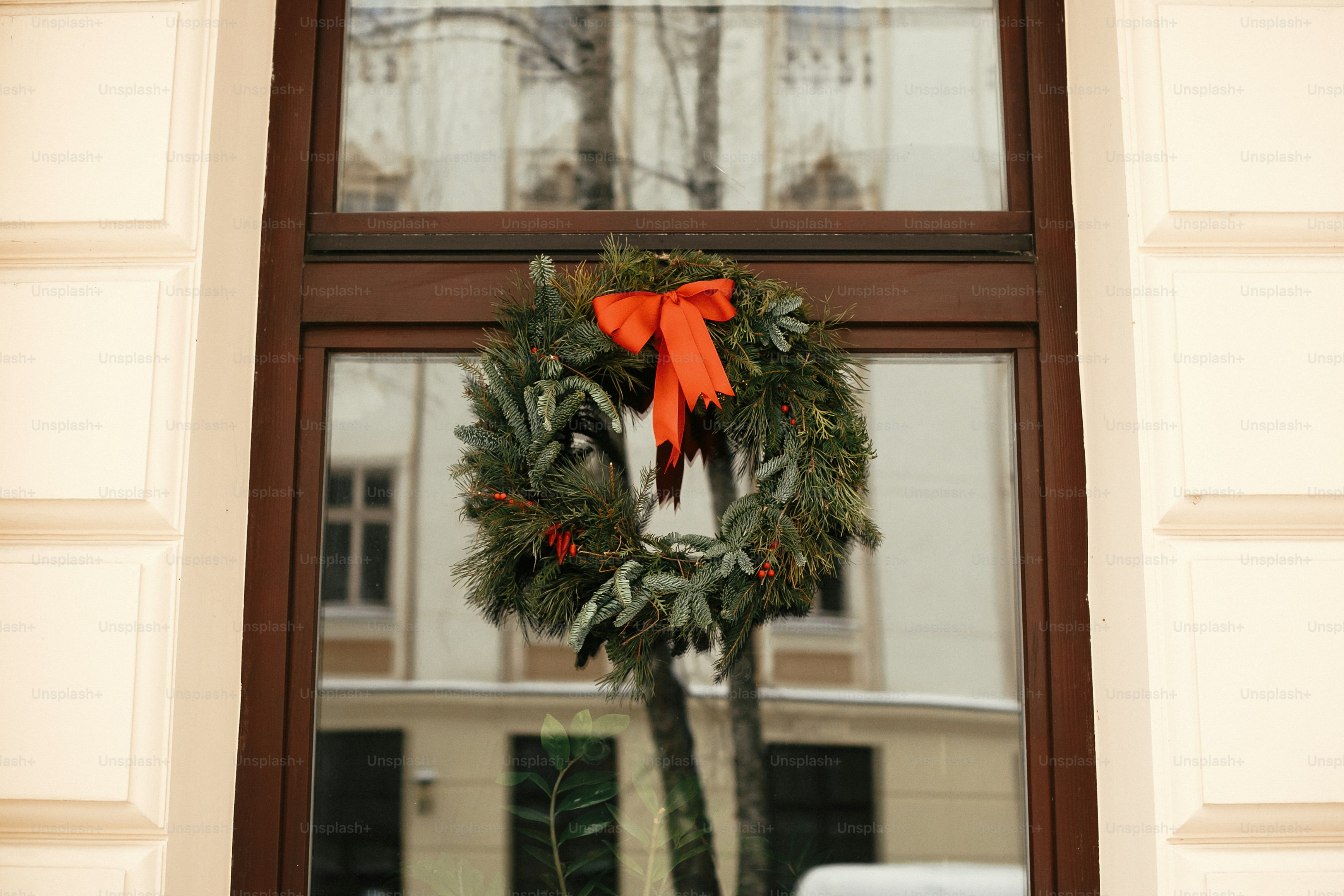 Christmas street decor. Stylish christmas wreath with red bow and berries at front of store at holiday market in city street. Space for text. Rustic decoration