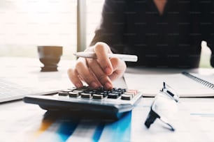 Close up Business woman using calculator and laptop for do math finance on wooden desk in office and business working background, tax, accounting, statistics and analytic research concept