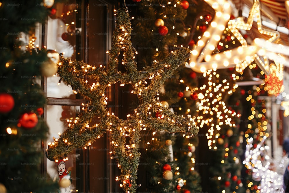 Estrela de Natal elegante iluminada e ramos de abeto com enfeites vermelhos e dourados, luzes douradas bokeh na frente do edifício no mercado de férias na rua da cidade. Decoração de rua de Natal