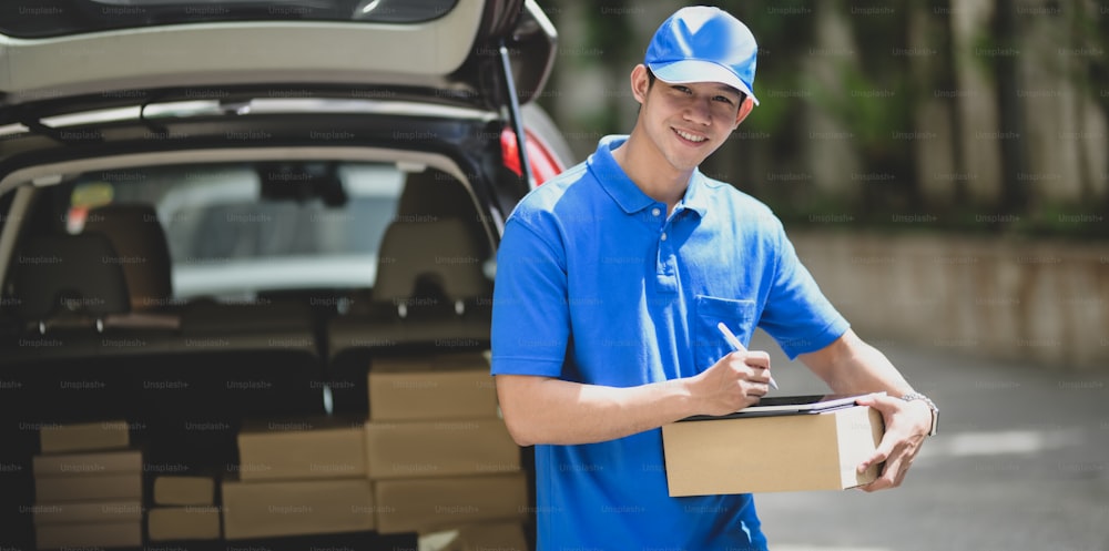 Young delivery man checking the products to customer while standing right next to his car and smiling to the camera.