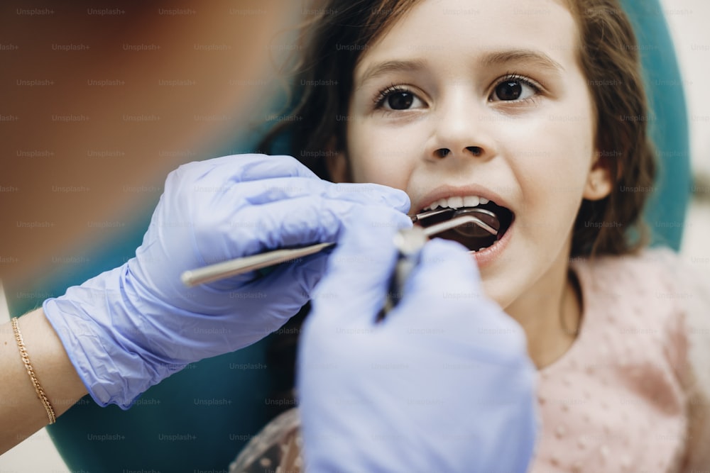 Gros plan d’une charmante petite fille assise dans un fauteuil de stomatologie, la bouche ouverte lors d’un examen dentaire par un dentiste pédiatrique.