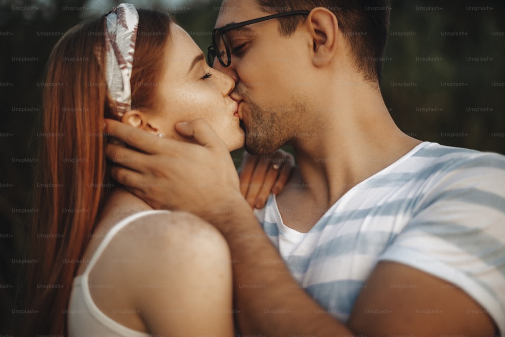 남자가 데이트하는 동안 야외에서 손으로 여자 친구의 얼굴을 만지고 있는 동안 눈을 감고 키스하는 매력적인 커플의 클로즈업.