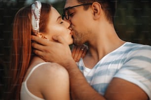 Close up of a charming couple kissing with closed eyes while man is touching face of her girlfriend with hand outdoor while dating.