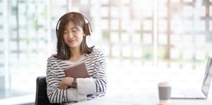 Young adorable female holding a book while listening to her favourite music in workplace