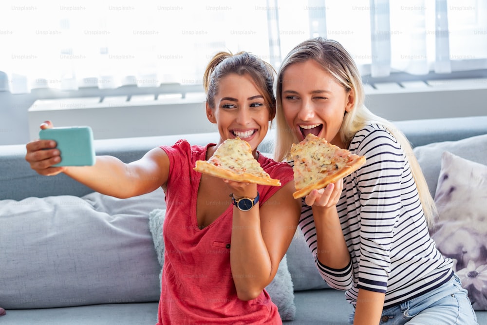 Freunde essen Pizza und lächeln für Selfies. Sie teilen Pizza und machen Selfie-Fotos auf dem Smartphone.