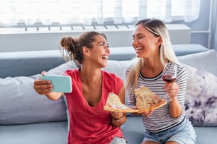 Amici che mangiano pizza e sorridono per un selfie. Condividono la pizza e fanno foto selfie sullo smartphone.