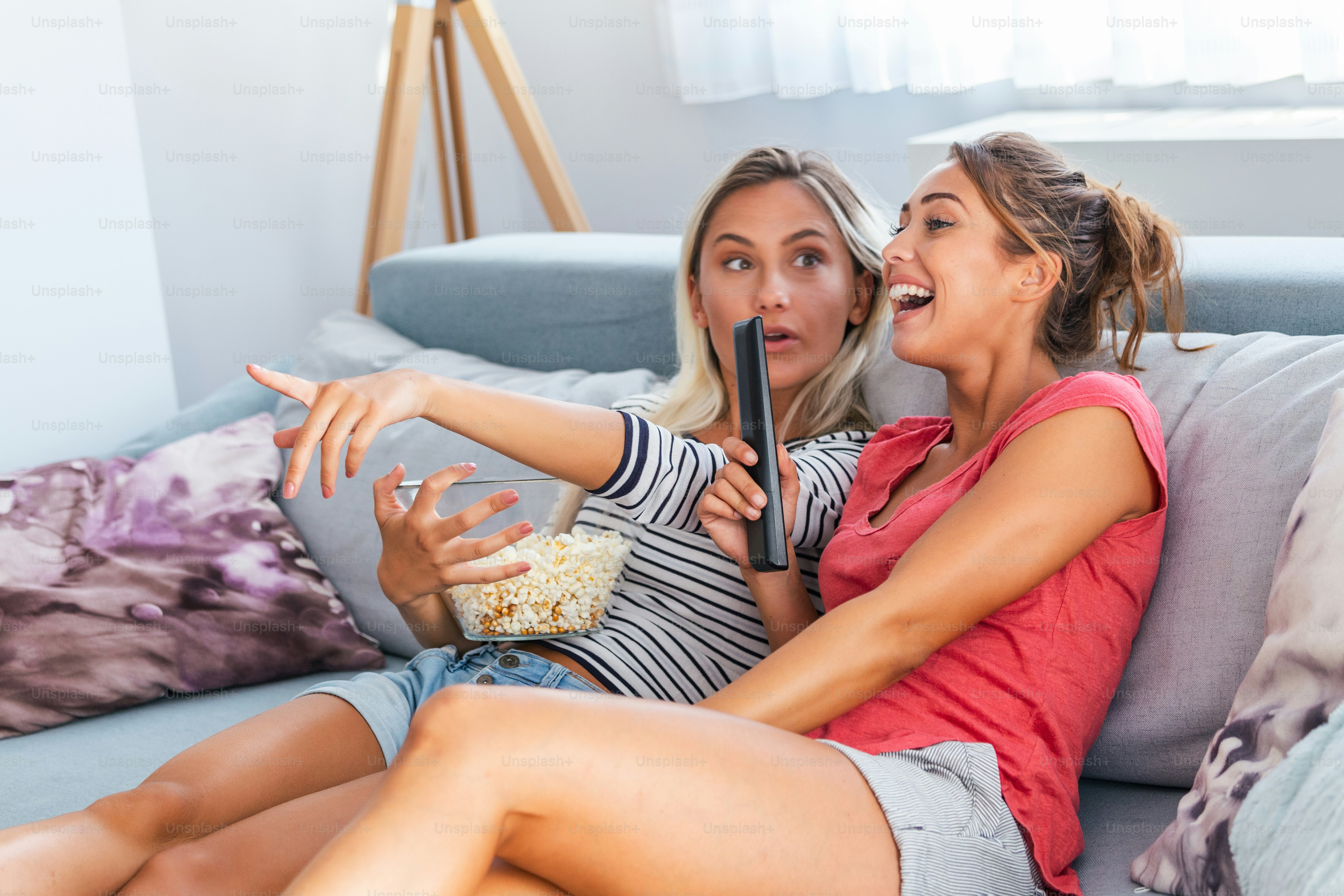 Portrait of funny and happy young women watching comedy in bed and  laughing. Cheerful friends eating tasty popcorn and looking movie with  gladness. Cozy and friendly atmosphere photo – Living room Image, image size:3000x2000