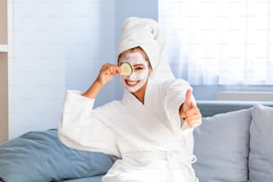 Young woman with clay facial mask holding cucumber slices. Beautiful young woman with facial mask on her face holding slices of fresh cucumber. Skin care and treatment, spa, natural beauty and cosmetology concept