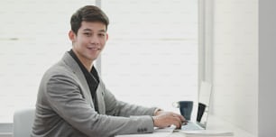 Portrait of young businessman smiling to the camera while working on his project in modern workplace