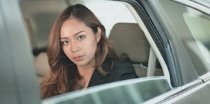 Beautiful businesswoman sitting at the back set of her car while heading to the office.