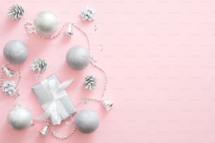 Décorations de Noël en argent, boules, boîte-cadeau, pommes de pin sur fond rose pastel. Composition minimale de Noël avec un décor de luxe moderne. Mise à plat, vue de dessus, espace de copie