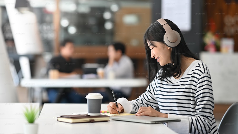 Young creative woman writing and listening music in modern office.
