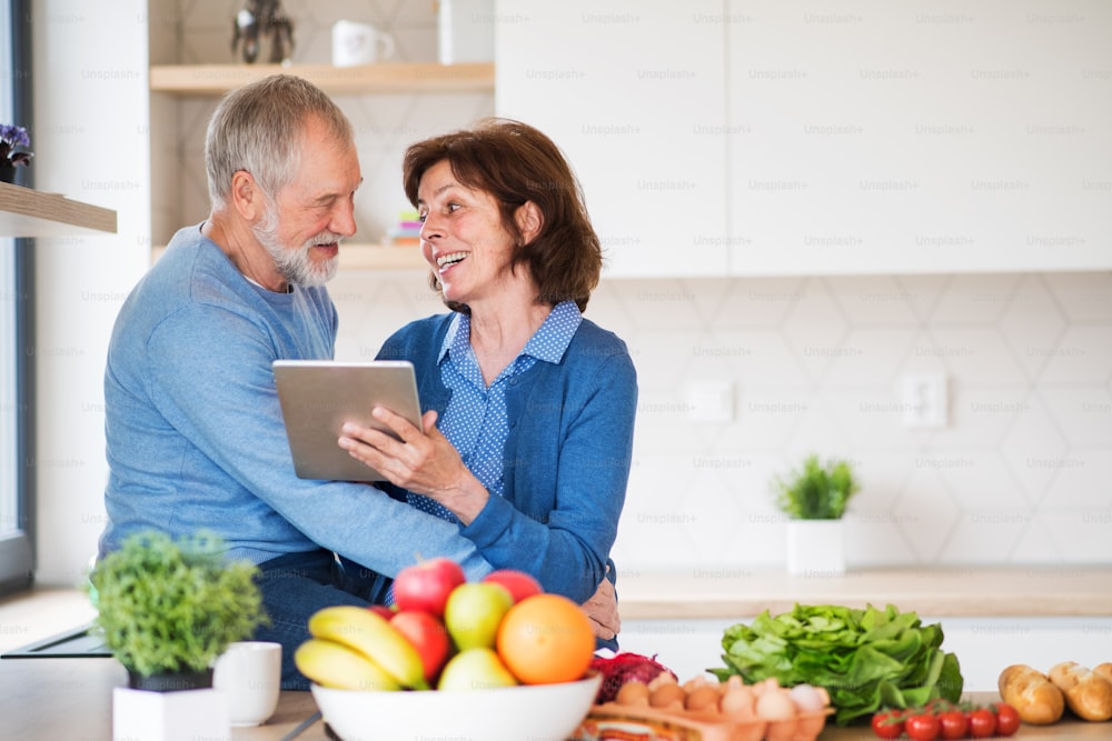 Ein Porträt eines glücklichen älteren Paares, das zu Hause verliebt ist und mit Tablet nach einem Rezept sucht.