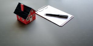 Conceito de investimento imobiliário e imobiliário: modelo de casa pequena com papel de nota e caneta no fundo cinzento