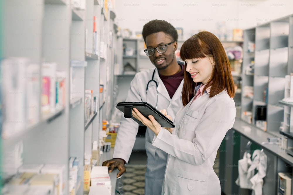Confident Male And Female Pharmacists In Pharmacy. female pharmacist talking with her colleague about the attributes and side effects of a medicine or pharmaceutical product for sale, in the pharmacy.
