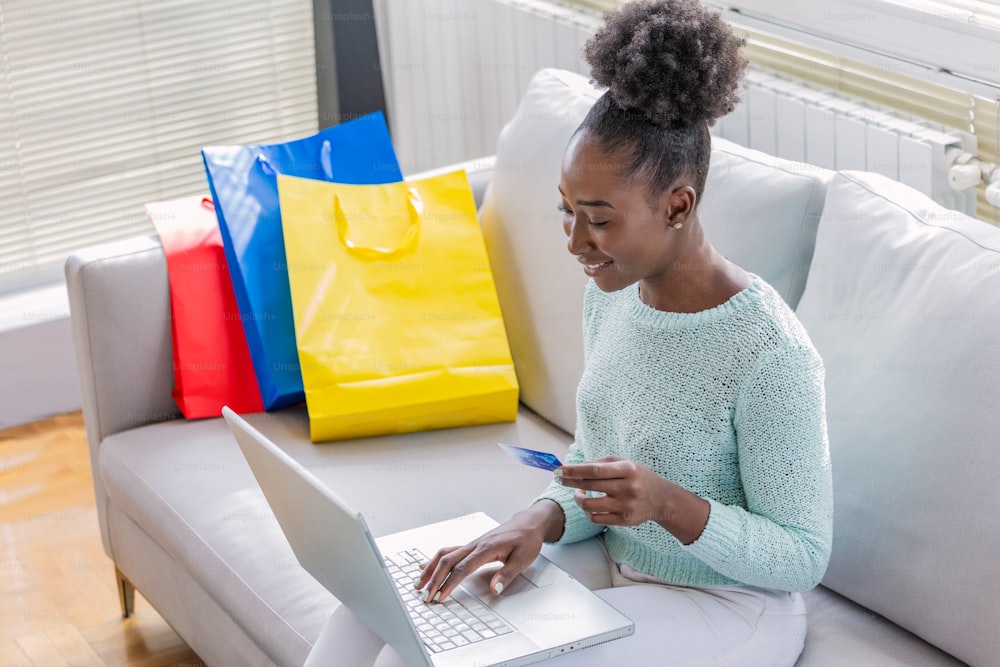 Mulher negra bonita fazendo compras on-line com cartão de crédito. Mulher segurando o cartão de crédito e usando o laptop. Conceito de compras online