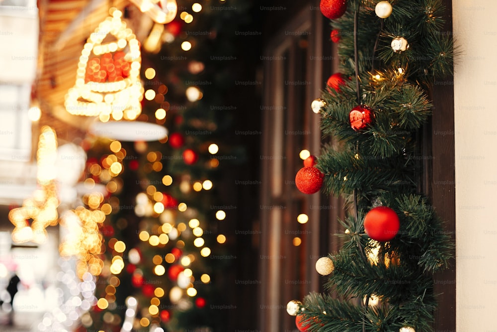 金色のライトが付いている流行のクリスマスのもみの枝、都市の通りの休日の市場の窓の店の赤いお祝いのつまらないもの。クリスマスの通りの装飾。テキスト用のスペース。