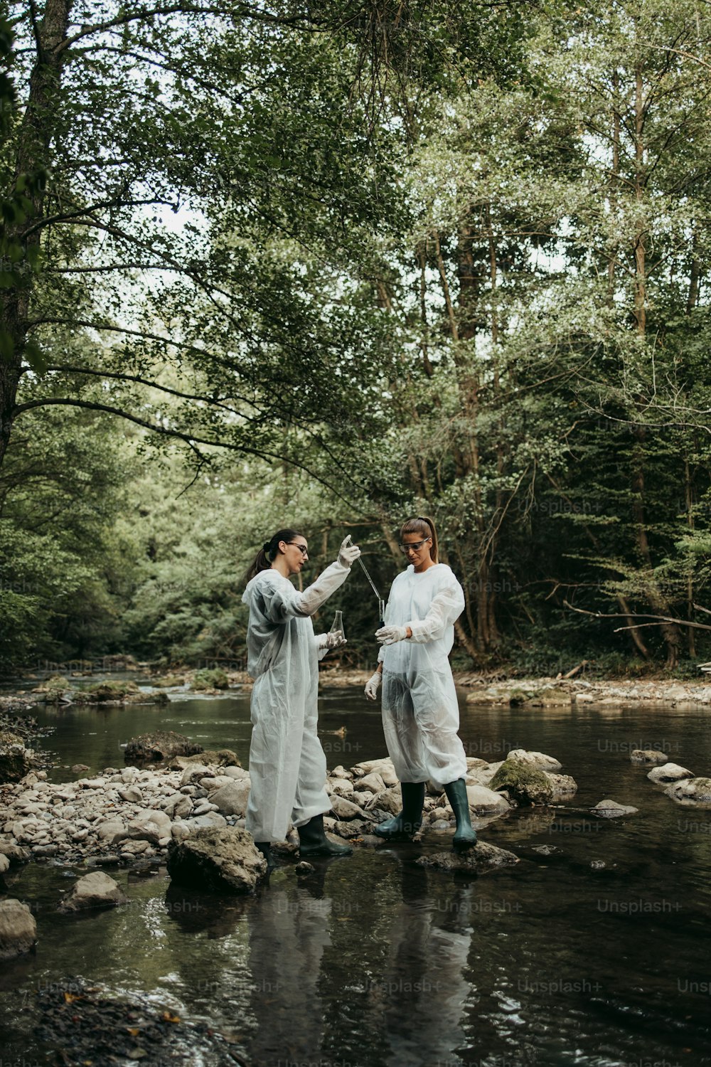 Scientists biologists and researchers in protective suits taking water samples from polluted river.