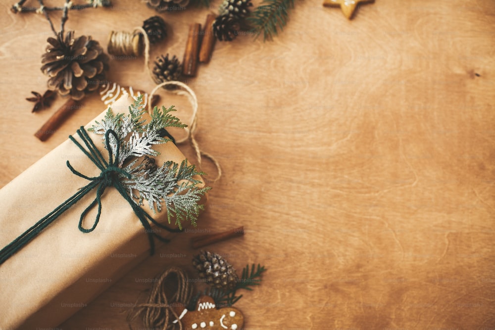 Elegante scatola rustica per regali di Natale con ramo di cedro su tavolo rurale in legno con pigne, biscotti di pan di zenzero, cotone, cannella. Testo spazio. Buone feste. Buon Natale.