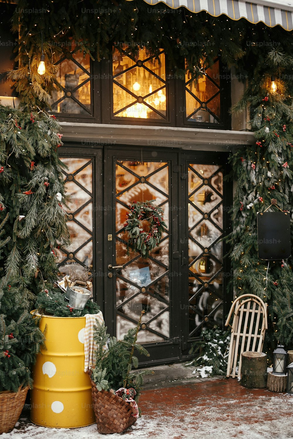 Weihnachtliche Straßendekoration. Stilvoller Weihnachtsbaum mit roten Beeren, Kranz an Türen und Holzschlitten vor dem Geschäft auf dem Weihnachtsmarkt in der Stadtstraße. Platz für Text. Rustikale Dekoration