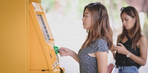 Dos jóvenes asiáticas retiran el dinero de una tarjeta bancaria usando un cajero automático en el centro comercial