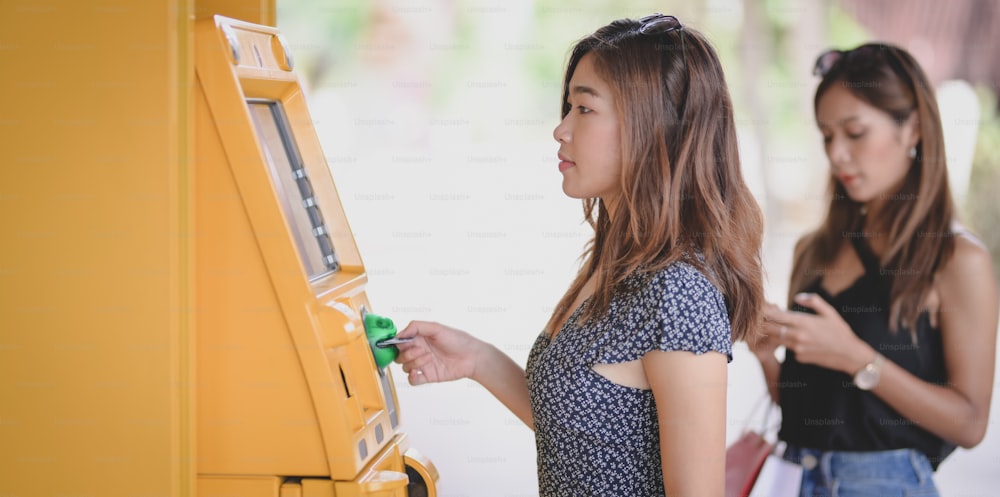 Two young asian female withdrawing the money from a bank card using ATM machine at the mall