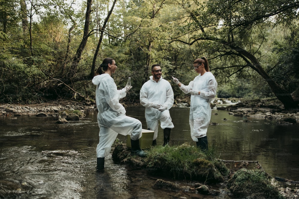 보호 복을 입은 과학자 생�물 학자와 연구원이 오염 된 강에서 물 샘플을 채취합니다.
