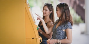 Two beautiful asian female withdrawing the money from a bank card using ATM machine at the mall