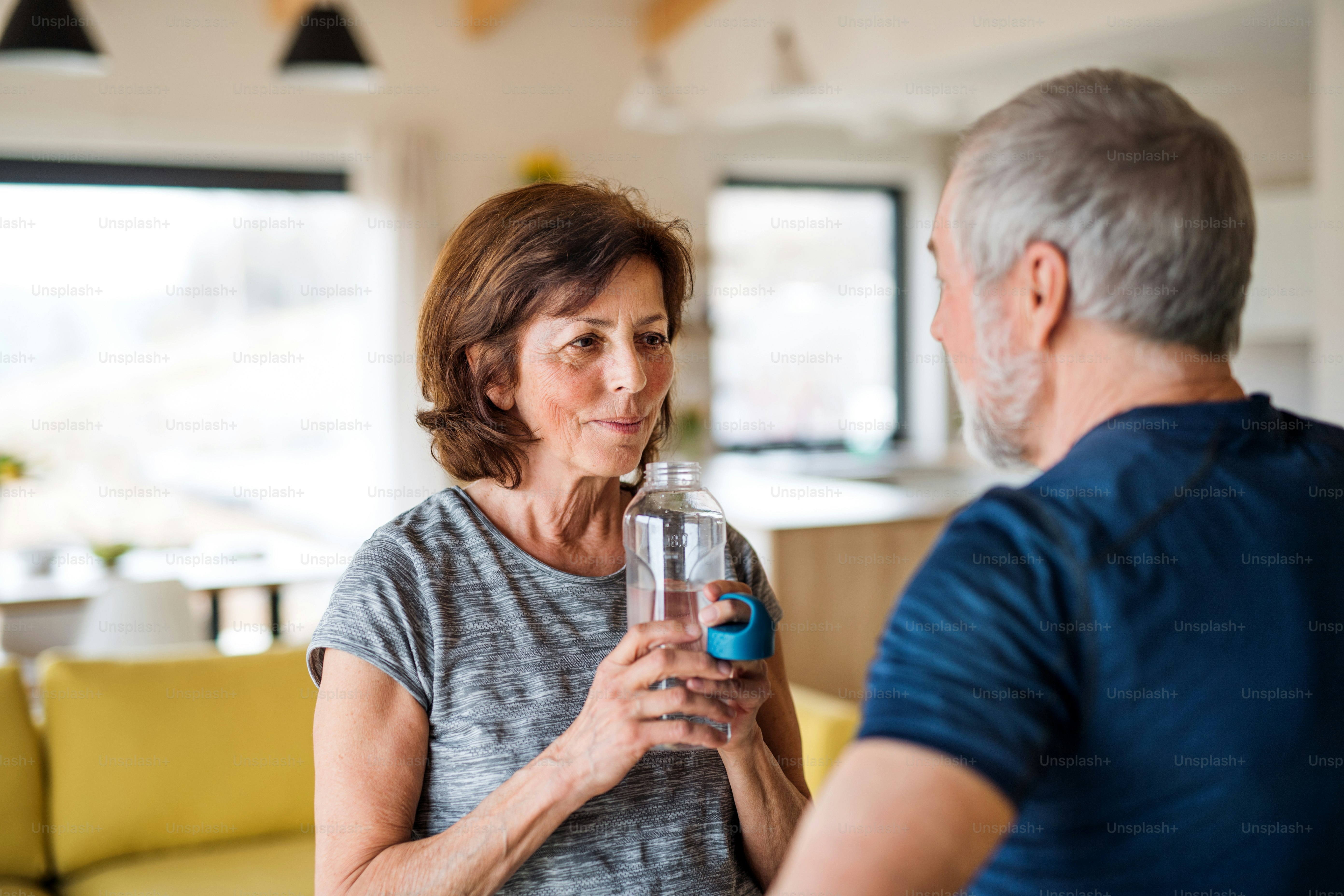 A happy senior couple indoors at home, resting after doing exercise indoors
