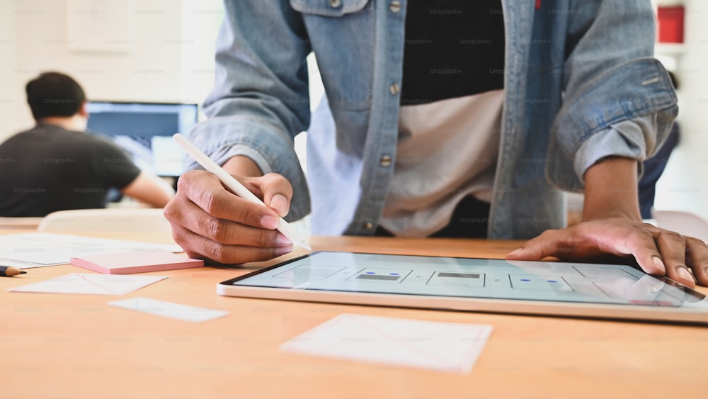 Nahaufnahme junger Entwickler, der ein UX-UI-Projekt auf einem digitalen Tablet entwirft.