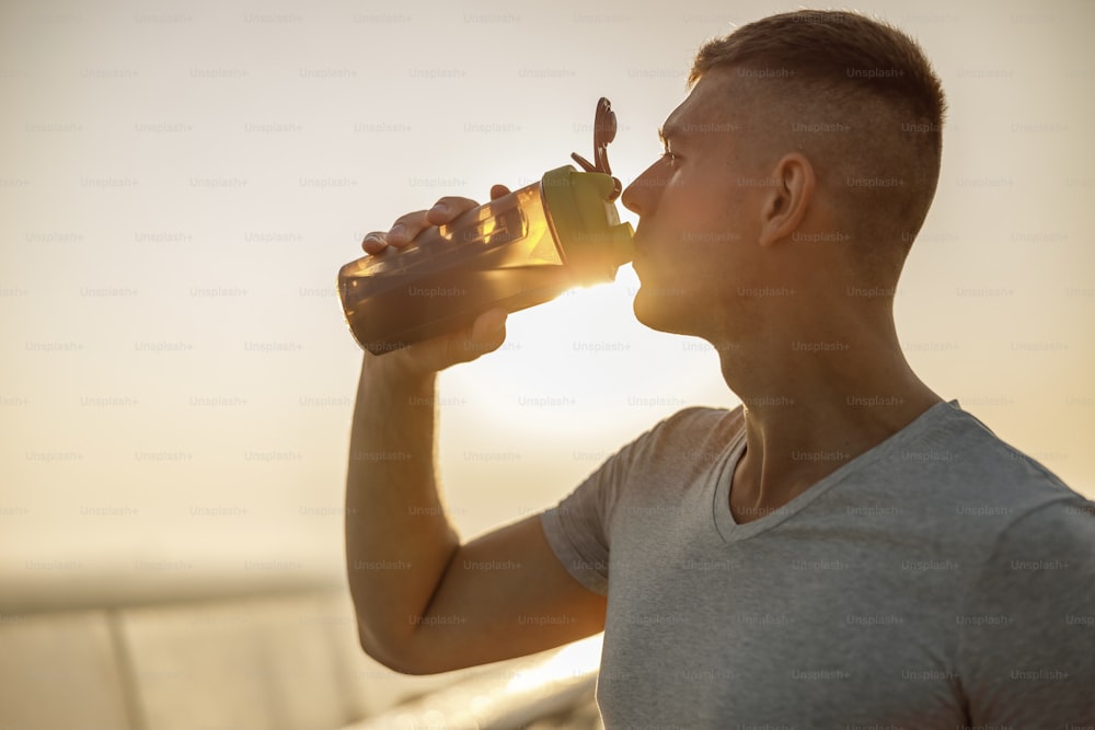 Closeup portrait of a handsome muscular young man drinking water from a plastic bottle