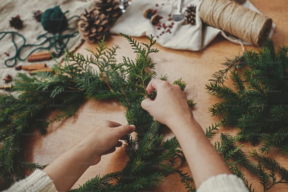 전나무 가지와 소나무 콘, 실, 열매, 나무 테이블에 가위를 들고 손. 크리스마스 화환 워크숍. 정통 세련 된 정물. 소박한 크리스마스 화환 만들기.
