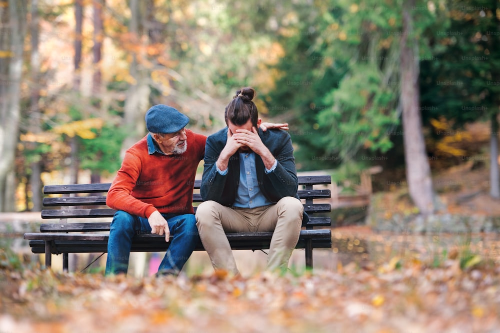 Un père âgé réconforte son fils adulte triste et frustré sur un banc dans la nature.