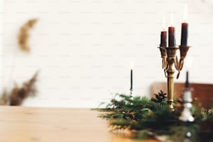 Elegante arreglo navideño rústico para la cena festiva. Ramas de abeto con piñas y candelabro vintage con velas negras sobre mesa de madera. Espacio de copia. Decoración de mesa rural navideña