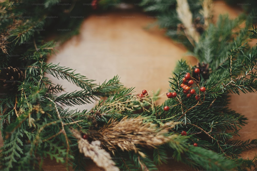 Rustikale Weihnachtskranz Detail Nahaufnahme. Tannenzweige, Tannenzapfen, Beeren auf Holztisch. Authentisches stilvolles Stillleben. Weihnachtskranz machen.