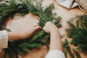 素朴なクリスマスリース作り。モミの枝、松ぼっくり、糸、果実、木のテーブルの上のハサミを持つ手。クリスマスリースワークショップ。本物のスタイリッシュな静物画