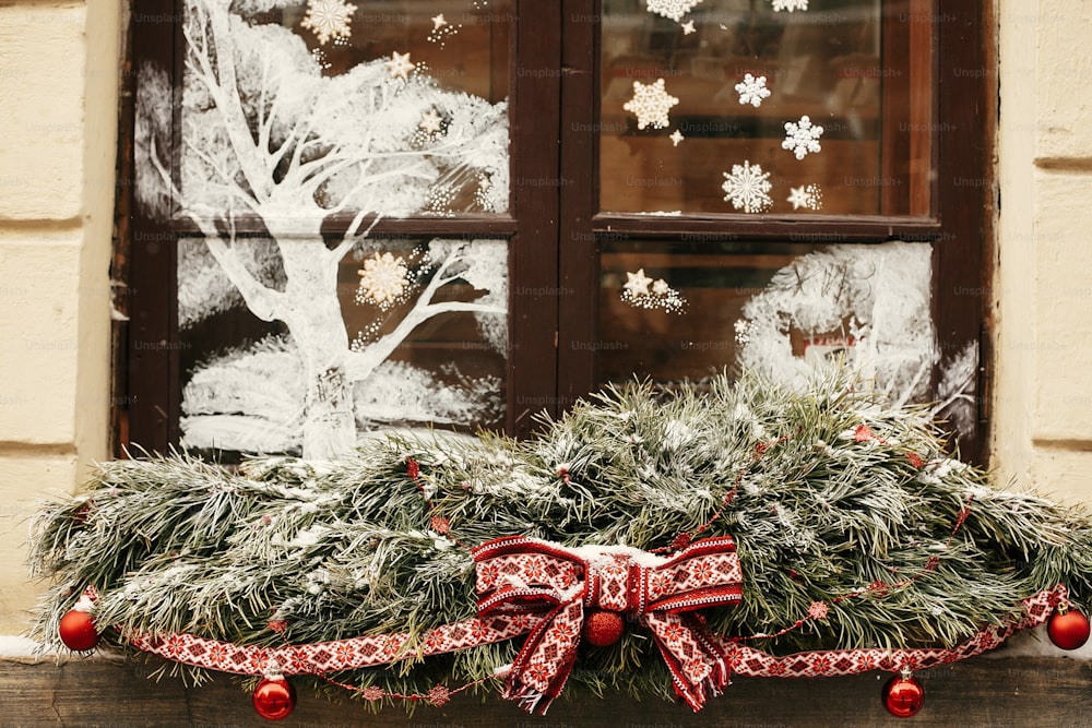 Decoración navideña de la calle. Elegantes ramas de abeto nevado de Navidad con lazo rojo festivo y bolas en la tienda de escaparates en el mercado de vacaciones en la calle de la ciudad. Espacio para el texto.