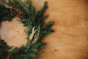 Ghirlanda rustica di Natale a posa piatta. Ghirlanda natalizia rurale creativa con rami di abete, bacche, pigne ed erbe aromatiche su tavolo di legno. Copia spazio. Auguri di buone feste