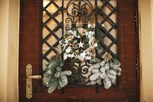 Decoración navideña de la calle. Elegante corona rústica navideña con piñas y estrella blanca en la puerta principal de la tienda en el mercado navideño en la calle de la ciudad. Espacio para el texto. Decoración rústica