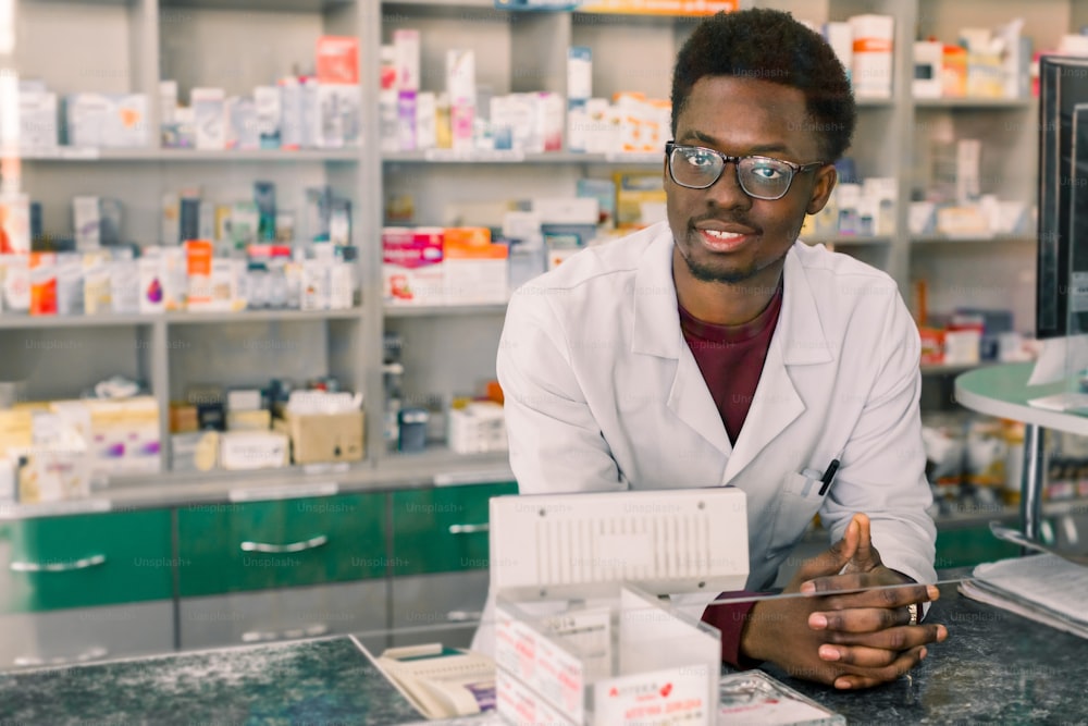 Experienced African American man pharmacist in white coat working in modern pharmacy.