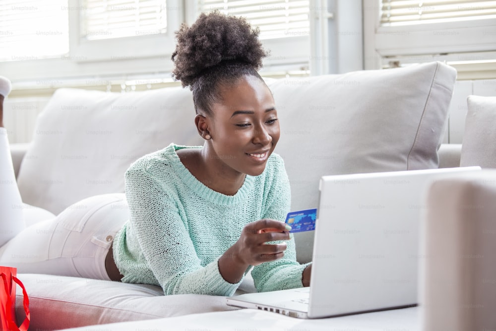 Imagem mostrando mulher bonita fazendo compras on-line com cartão de crédito. Mulher afro-americana segurando cartão de crédito e usando laptop. Conceito de compras online